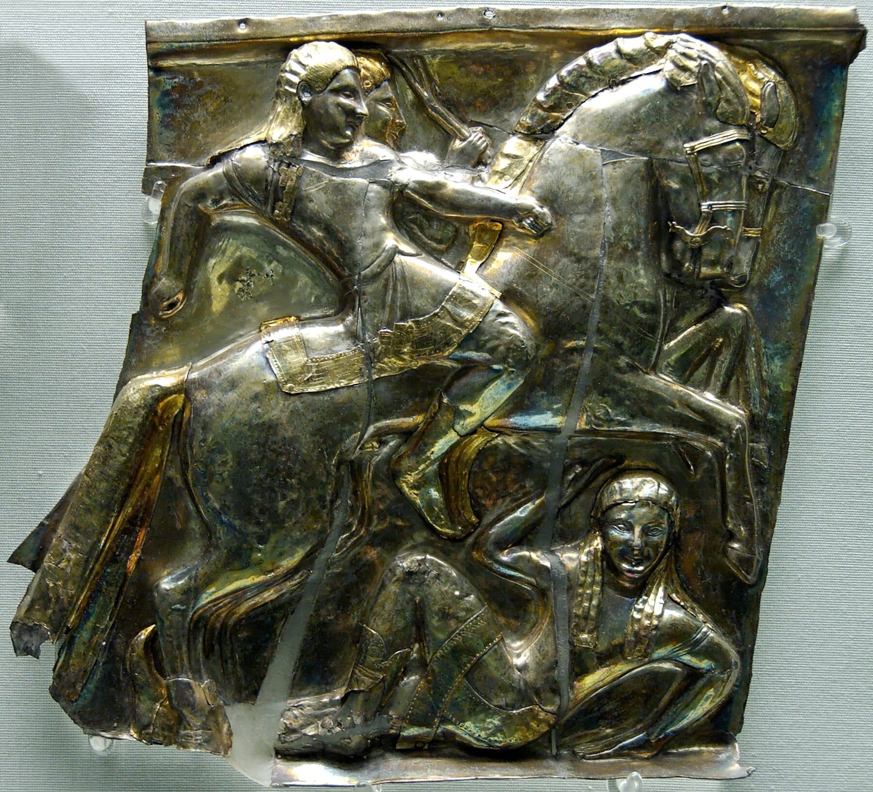 An Archaic Etruscan silver panel showing riders and animals in low relief, the figures raised from the sheet in repoussé and overlaid with pale electrum foil.