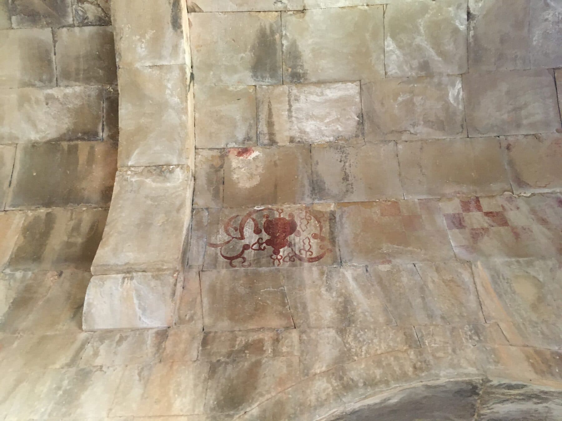 Deep crimson vegetal ornaments painted on a weathered stone-and-plaster ceiling.