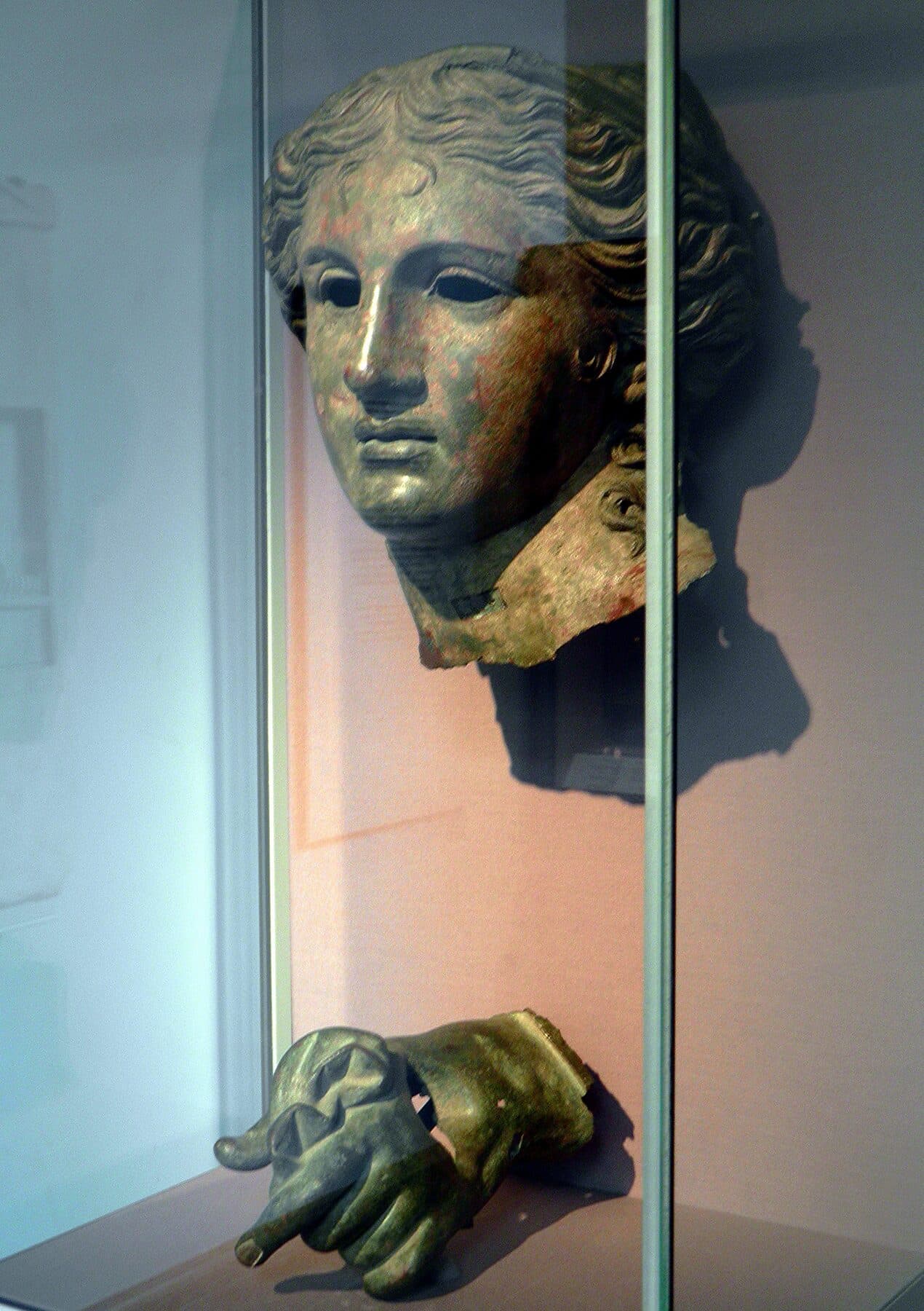 A three-quarter view of the bronze head of Anahita, showing the modelled cheek, lips, and the empty sockets where the eyes were once inlaid.