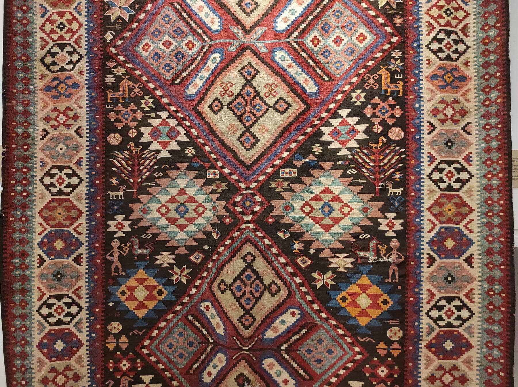 An Armenian flatweave carpet patterned with stylized trees, diamond medallions, and small woven human and animal figures.