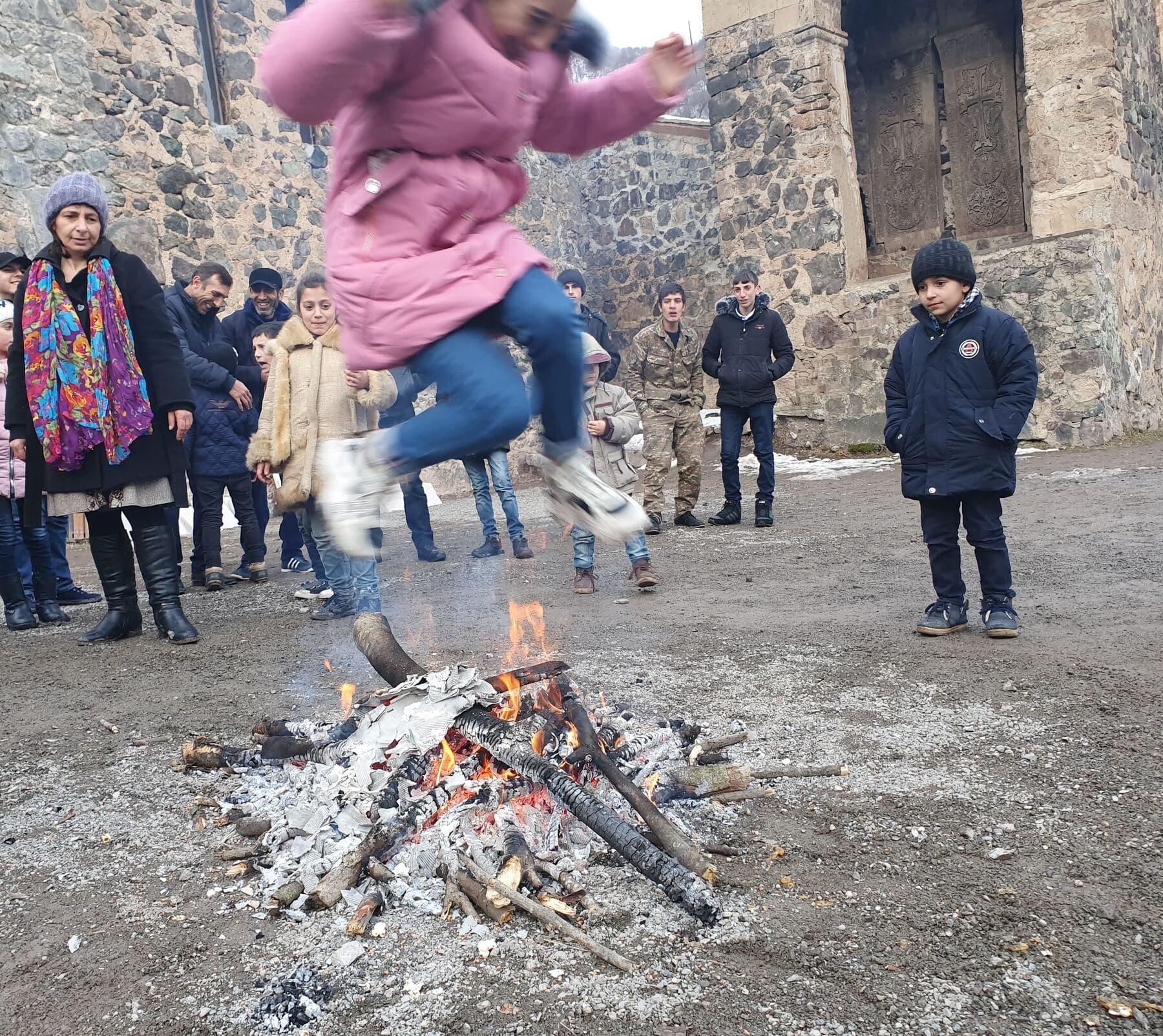 A nighttime Trndez bonfire at Dadivank monastery, its flames lighting a circle of onlookers in the snow.