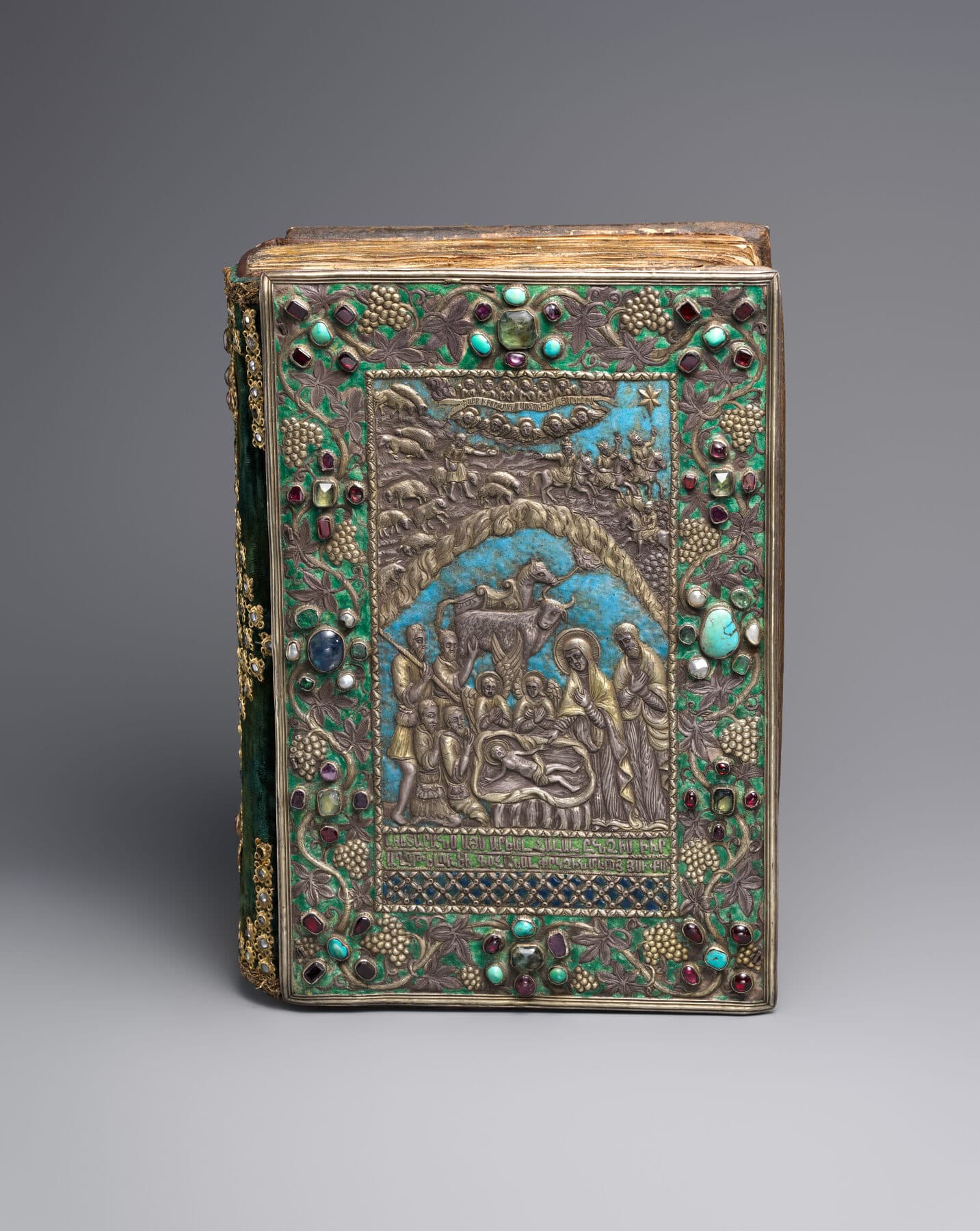 An Armenian Gospel book with a gilded-silver cover worked in repousse, set with coloured enamels and jewels around a central figural panel.