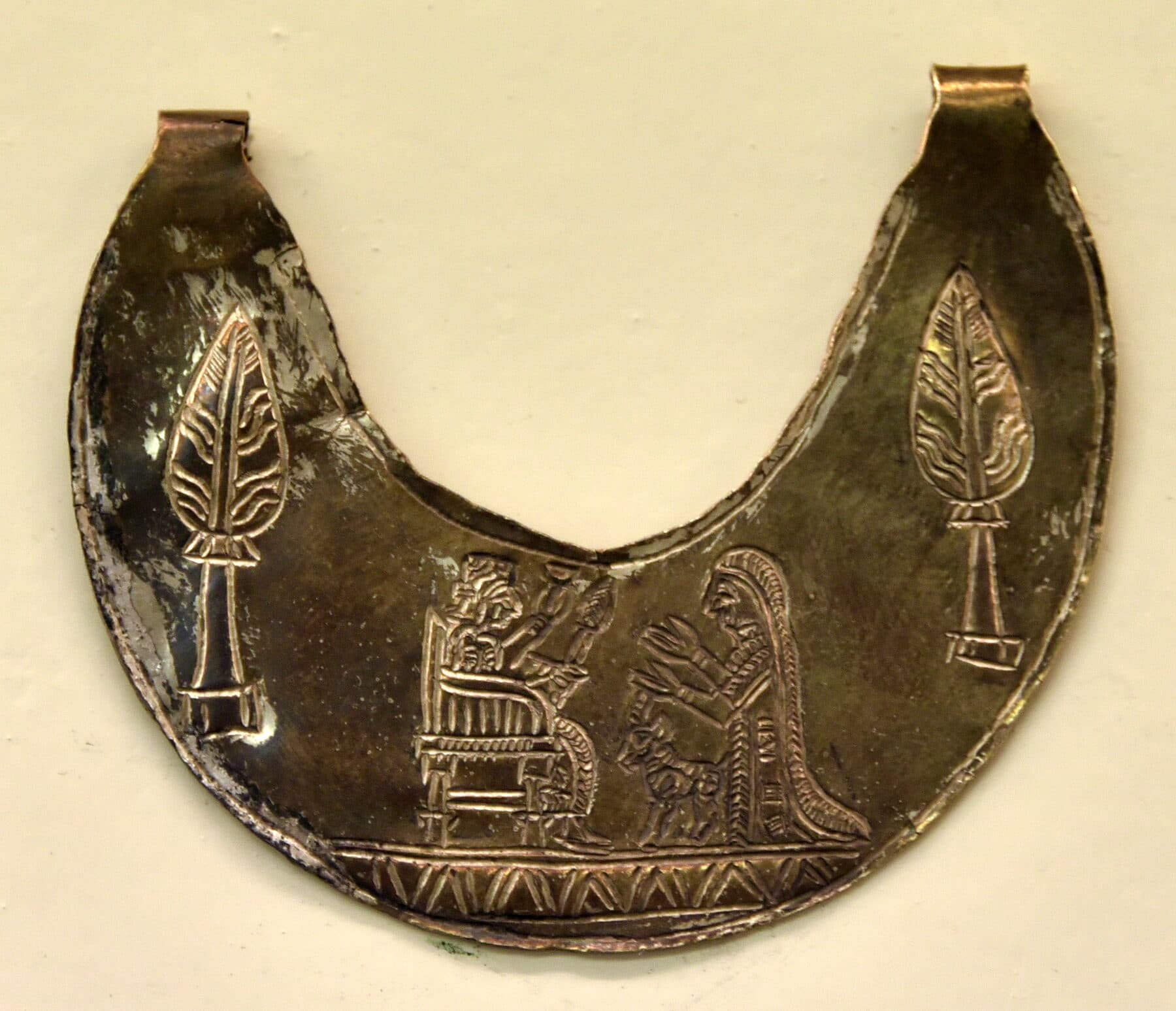 A crescent-shaped gold-and-silver Urartian pectoral engraved with a worshiper before an enthroned deity, flanked by two stylized trees.