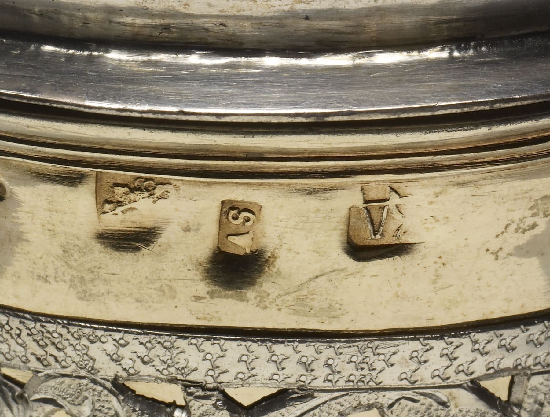 An extreme close-up of a struck mark stamped into the silver surface of a Russian covered cup — a small punched device pressed into the metal.